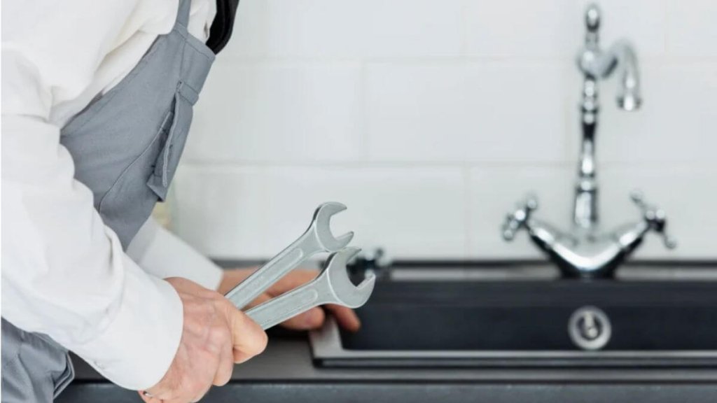 A professional plumber holding two wrenches beside a kitchen sink.