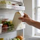 An open refrigerator in a bright Australian kitchen with a person's hand reaching in to hold a plain unlabelled carton, shelves of everyday groceries with no readable labels, soft natural light from a nearby window.