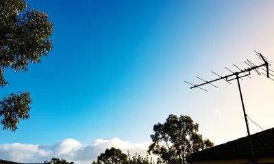 A clear bright-blue Australian sky seen over eucalyptus tree tops with a Hills hoist clothesline silhouetted in the lower frame and soft white clouds on the horizon.