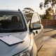 Right-hand-drive compact SUV parked in a suburban car hire yard in late afternoon light, one front door open with a set of keys hanging from the handle and a clipboard with a blank condition sheet on the bonnet