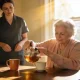 Elderly woman pouring tea at a kitchen table while a younger carer stands one step behind in a bright Australian home