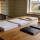 Two stacks of blank paperwork, a folder and pen, a pot of tea and two closed passports on a timber table in late afternoon light, with a weatherboard wall and suburban garden behind