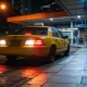 taxi pulling up on a night-time city street with a waiting person