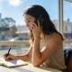 Woman making notes in a notebook during a phone call at a sunlit Melbourne cafe table