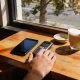 Hand resting between a modern smartphone and a simple keypad phone on a timber cafe table, weighing the switch