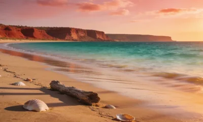 Empty tidal sand and calm shallow water at a remote Northern Territory beach at golden hour, low red-ochre cliffs in the distance