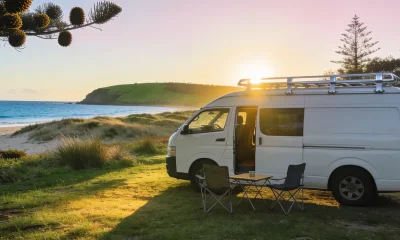 White campervan parked at a quiet beachfront campground on Australia's east coast in early morning light, coastal headland and ocean in the background