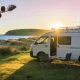 White campervan parked at a quiet beachfront campground on Australia's east coast in early morning light, coastal headland and ocean in the background