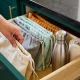 Hand lifting a folded reusable shopping bag from a kitchen drawer holding a stainless bottle and cloth bags.
