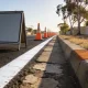 Fresh white edge line and worn older road markings on a suburban Australian street, a row of orange traffic cones receding into the distance and a blank roadworks sign on the road shoulder beside dry verge grass