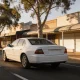 A white taxi driving along a quiet country-town main street in the afternoon.