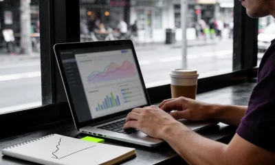 Small-business owner working on a marketing plan at a cafe window table with a laptop and notebook.