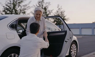 A driver helping an older passenger out of a car outside a medical centre in the morning.