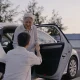 A driver helping an older passenger out of a car outside a medical centre in the morning.