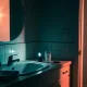 Dimly lit Australian bathroom seen from the doorway at night, with a glass of milk, a small lit torch and a car key on the vanity beside a round mirror and folded towel, warm light spilling in from the hall