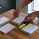 Hands sorting blank papers into three neat piles with a pen and yellow highlighter on a warm timber kitchen table.