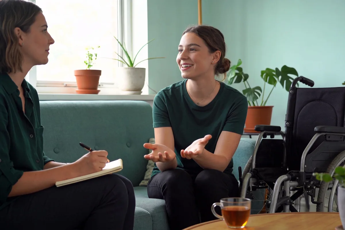 A support coordinator and a young woman having an NDIS planning conversation in a bright home living room.