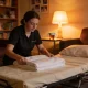 NDIS support worker making up a fold-out bed in a softly lit Australian lounge at night during a sleepover shift
