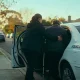 A support worker helping a man with a walking cane into an unmarked white car on a quiet suburban Melbourne street in early morning light.