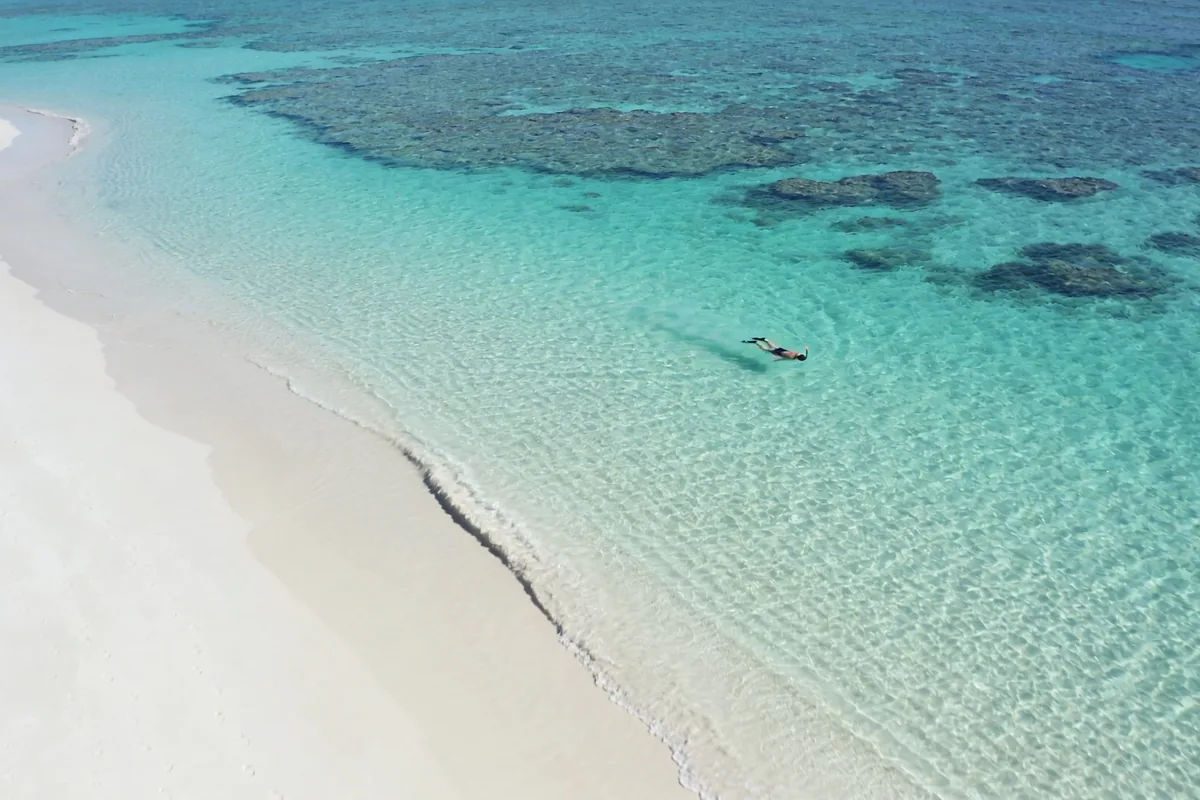 Calm shallow turquoise bay on the Ningaloo coast with white sand at the water's edge and the reef visible as darker patches just offshore