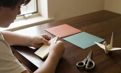 child folding origami with scissors and paper at a wooden table