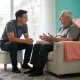 Care worker seated at eye level listening to an older man in an armchair in a light-filled Australian lounge