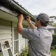 A pest technician inspecting the roofline of a suburban Melbourne home in daylight.