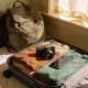 Open suitcase on a bed with a mirrorless camera and a smartphone side by side among folded clothes