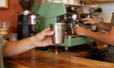 Customer at a local cafe counter holding out a plain stainless reusable coffee cup to the barista.