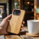 Hand holding a smartphone in a bamboo-backed phone case with raised corners on an outdoor Melbourne cafe table in natural light.