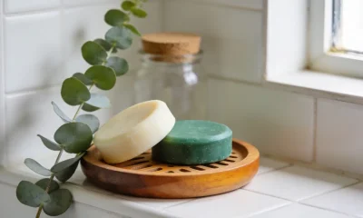 Two solid shampoo and conditioner bars on a small wooden dish in a bright Australian bathroom, a sprig of eucalyptus beside them.