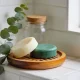 Two solid shampoo and conditioner bars on a small wooden dish in a bright Australian bathroom, a sprig of eucalyptus beside them.