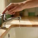 A hand reaching to turn off a dripping chrome kitchen tap in the morning light.