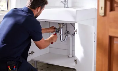 A plumber tightening pipework under a bathroom vanity in a bright Australian home.
