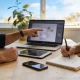 Two colleagues collaborating over a laptop, tablet and notebook at a sunlit home-office table.