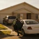 A car parked in a suburban driveway while a person opens the door of a waiting car at the kerb in the morning.