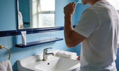 person gently brushing teeth at a bright bathroom basin