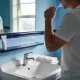 person gently brushing teeth at a bright bathroom basin