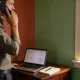 Consultant on a phone call beside an open laptop and notebook at a bright home-office desk.