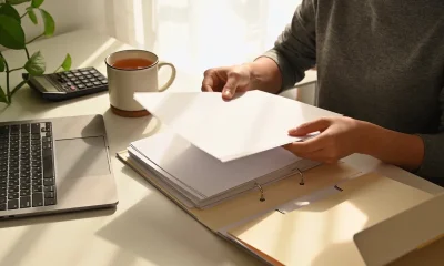 A person sorting blank papers into folders at a tidy home office desk in natural light.