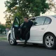 A passenger stepping into the back seat of a waiting car on a quiet suburban street in daylight.