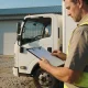A transport business owner reviewing paperwork beside a truck in a yard in daylight.