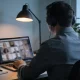Professional in headphones at a home-office desk during a video meeting on a laptop.