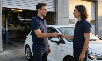 Service advisor handing car keys back to an owner beside a white European compact hatchback in a Melbourne service-centre forecourt
