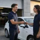 Service advisor handing car keys back to an owner beside a white European compact hatchback in a Melbourne service-centre forecourt