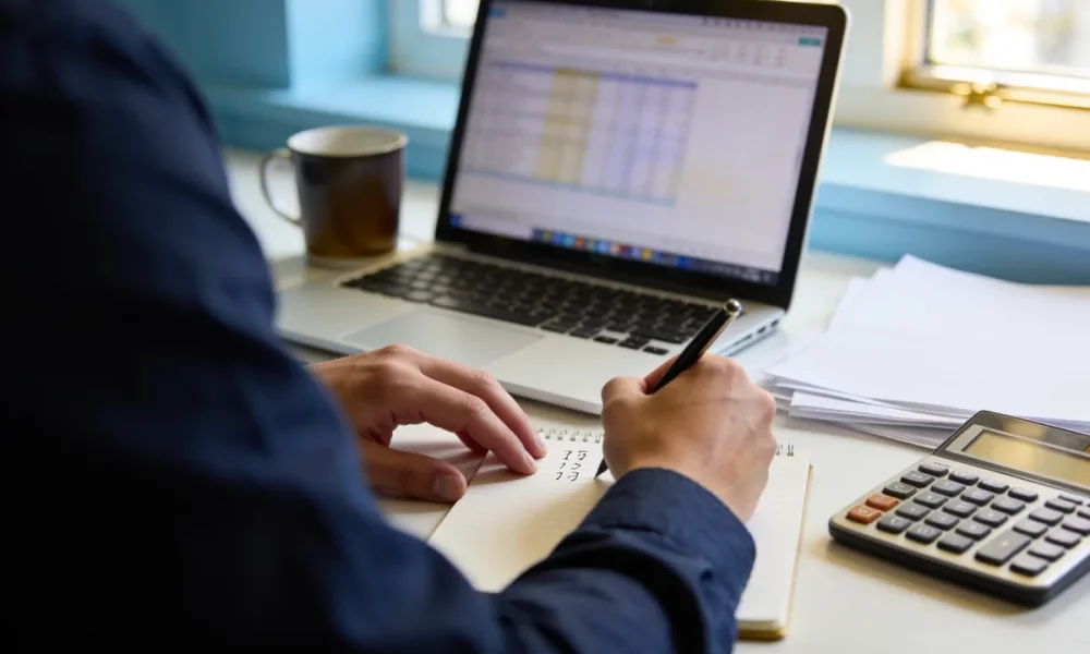 Person reviewing tax papers and figures with a calculator at a tidy home-office desk in the morning.