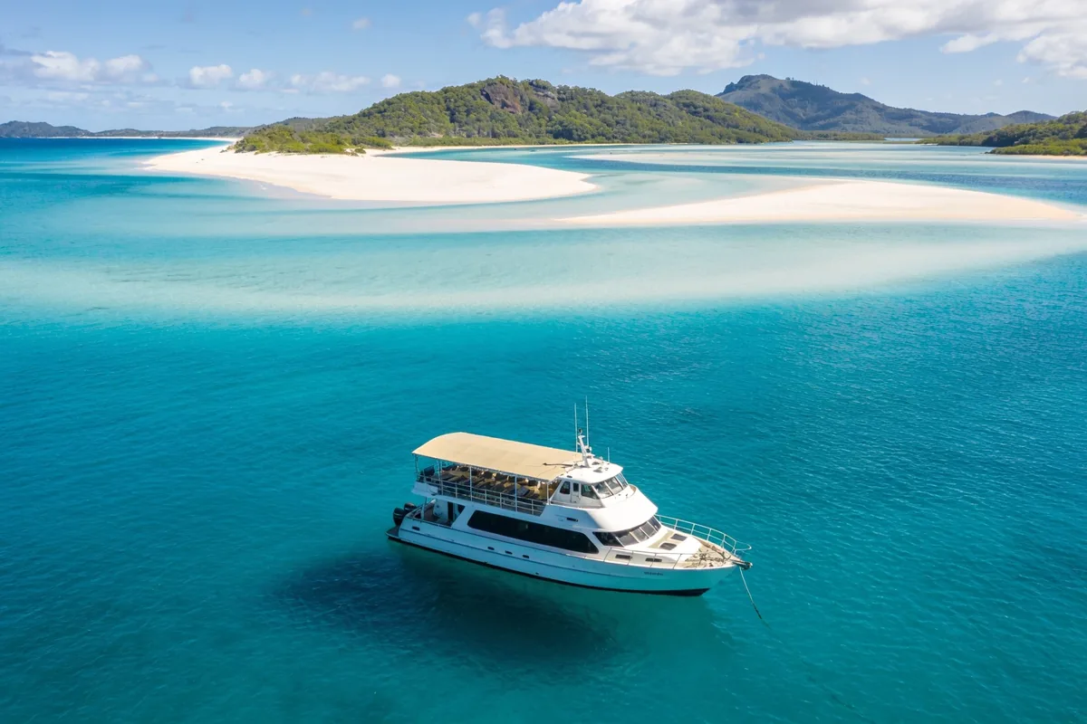 Small tour boat anchored in turquoise water in the Whitsundays, with the white sandbars of Whitehaven Beach and Hill Inlet in the background